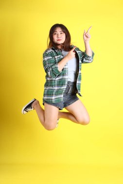 Sarı arka planda sıradan kıyafetlerle duran tombul Asyalı kadın..