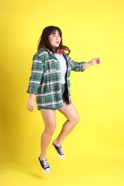 Sarı arka planda sıradan kıyafetlerle duran tombul Asyalı kadın..