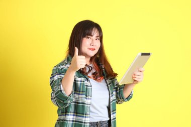 Sarı arka planda sıradan kıyafetlerle duran tombul Asyalı kadın..