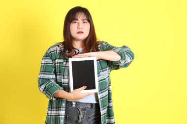 Sarı arka planda sıradan kıyafetlerle duran tombul Asyalı kadın..