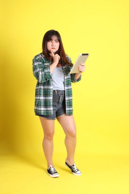 Sarı arka planda sıradan kıyafetlerle duran tombul Asyalı kadın..