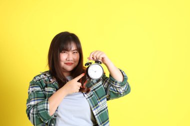 Sarı arka planda sıradan kıyafetlerle duran tombul Asyalı kadın..