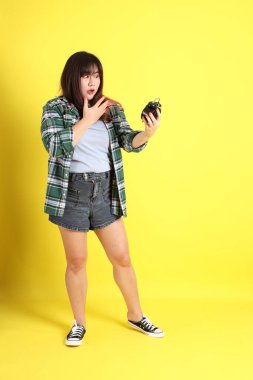 Sarı arka planda sıradan kıyafetlerle duran tombul Asyalı kadın..