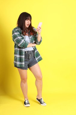 Sarı arka planda sıradan kıyafetlerle duran tombul Asyalı kadın..