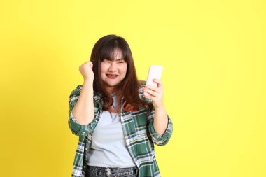 Sarı arka planda sıradan kıyafetlerle duran tombul Asyalı kadın..