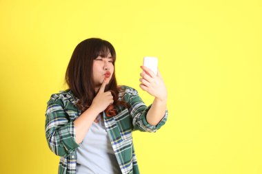 Sarı arka planda sıradan kıyafetlerle duran tombul Asyalı kadın..