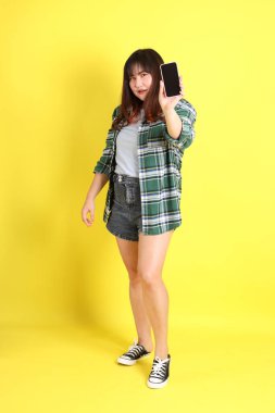 Sarı arka planda sıradan kıyafetlerle duran tombul Asyalı kadın..