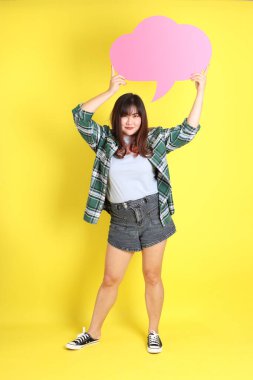 Sarı arka planda sıradan kıyafetlerle duran tombul Asyalı kadın..