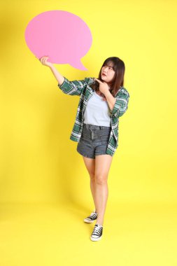 Sarı arka planda sıradan kıyafetlerle duran tombul Asyalı kadın..