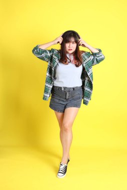 Sarı arka planda sıradan kıyafetlerle duran tombul Asyalı kadın..