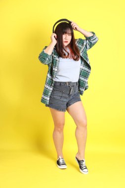 Sarı arka planda sıradan kıyafetlerle duran tombul Asyalı kadın..