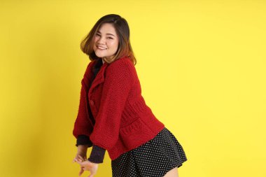 Sarı arka planda sıradan kıyafetlerle duran tombul Asyalı kadın..