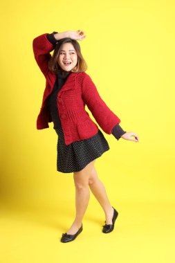 Sarı arka planda sıradan kıyafetlerle duran tombul Asyalı kadın..