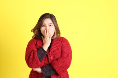 Sarı arka planda sıradan kıyafetlerle duran tombul Asyalı kadın..