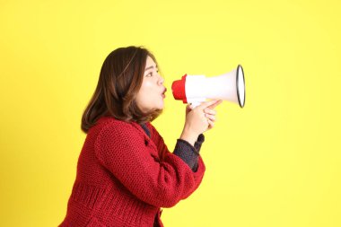The chubby Asian woman standing on the yellow background with the casual clothes.