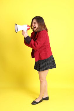 Sarı arka planda sıradan kıyafetlerle duran tombul Asyalı kadın..