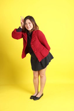 Sarı arka planda sıradan kıyafetlerle duran tombul Asyalı kadın..