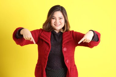 Sarı arka planda sıradan kıyafetlerle duran tombul Asyalı kadın..