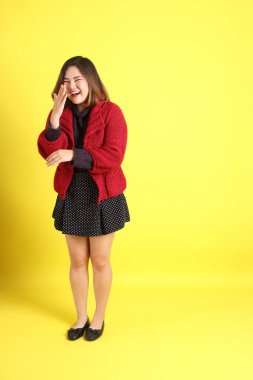 Sarı arka planda sıradan kıyafetlerle duran tombul Asyalı kadın..