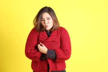 Sarı arka planda sıradan kıyafetlerle duran tombul Asyalı kadın..