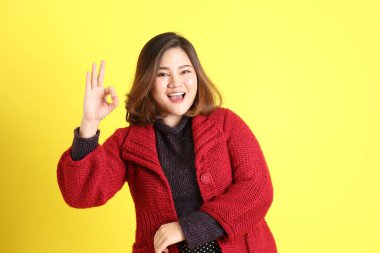 Sarı arka planda sıradan kıyafetlerle duran tombul Asyalı kadın..