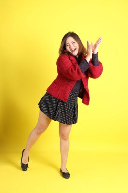 Sarı arka planda sıradan kıyafetlerle duran tombul Asyalı kadın..