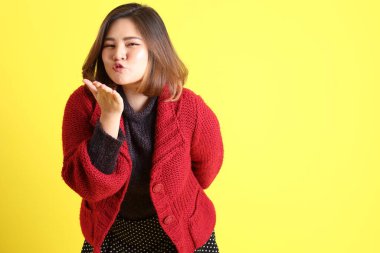 Sarı arka planda sıradan kıyafetlerle duran tombul Asyalı kadın..