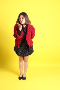 Sarı arka planda sıradan kıyafetlerle duran tombul Asyalı kadın..