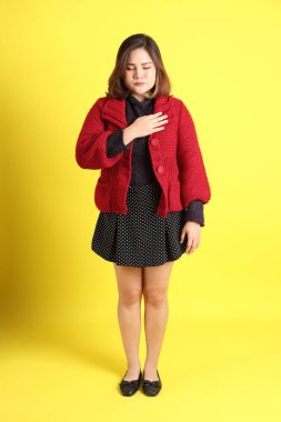 Sarı arka planda sıradan kıyafetlerle duran tombul Asyalı kadın..