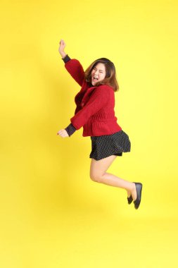 Sarı arka planda sıradan kıyafetlerle duran tombul Asyalı kadın..