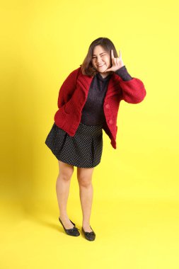 Sarı arka planda sıradan kıyafetlerle duran tombul Asyalı kadın..