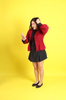 Sarı arka planda sıradan kıyafetlerle duran tombul Asyalı kadın..