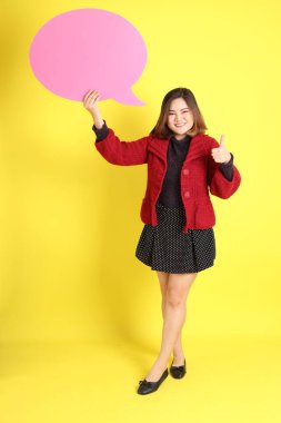 Sarı arka planda sıradan kıyafetlerle duran tombul Asyalı kadın..