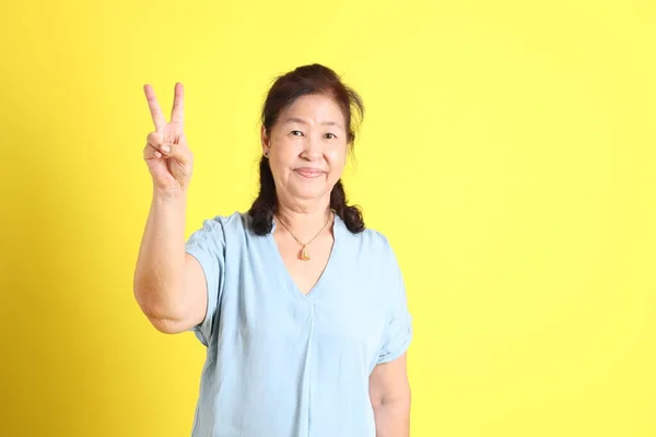 那位身穿浅蓝色衬衫的亚洲老妇人站在黄色的背景上 — 图库照片