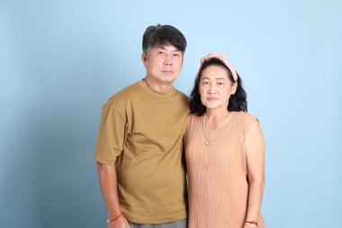 Mavi arka planda sıradan giysileri olan yakışıklı, son sınıf Asyalı çift..