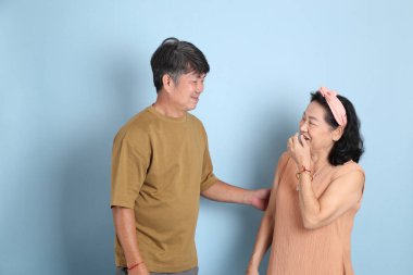 Mavi arka planda sıradan giysileri olan yakışıklı, son sınıf Asyalı çift..