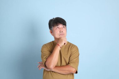 Mavi arka planda sıradan giyinmiş kıdemli Asyalı adam..