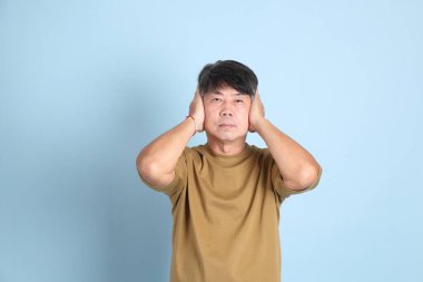 Mavi arka planda sıradan giyinmiş kıdemli Asyalı adam..