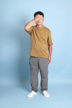 Mavi arka planda sıradan giyinmiş kıdemli Asyalı adam..