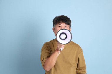 Mavi arka planda sıradan giyinmiş kıdemli Asyalı adam..