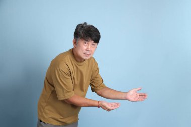 Mavi arka planda sıradan giyinmiş kıdemli Asyalı adam..