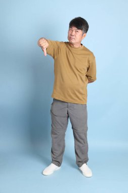 Mavi arka planda sıradan giyinmiş kıdemli Asyalı adam..