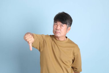 Mavi arka planda sıradan giyinmiş kıdemli Asyalı adam..