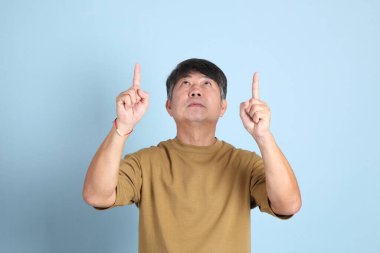 Mavi arka planda sıradan giyinmiş kıdemli Asyalı adam..