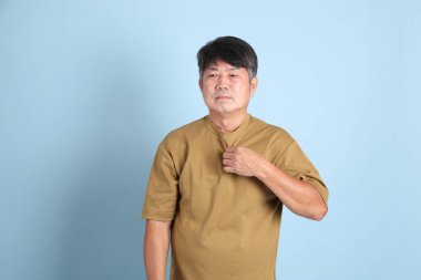 Mavi arka planda sıradan giyinmiş kıdemli Asyalı adam..