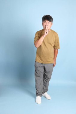 Mavi arka planda sıradan giyinmiş kıdemli Asyalı adam..