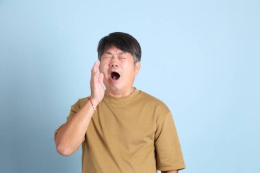 Mavi arka planda sıradan giyinmiş kıdemli Asyalı adam..