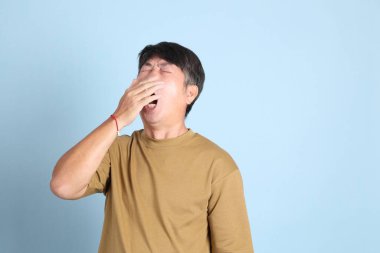 Mavi arka planda sıradan giyinmiş kıdemli Asyalı adam..