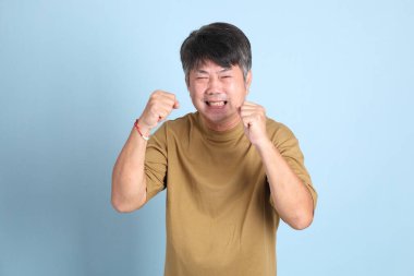 Mavi arka planda sıradan giyinmiş kıdemli Asyalı adam..