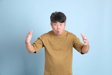 Mavi arka planda sıradan giyinmiş kıdemli Asyalı adam..